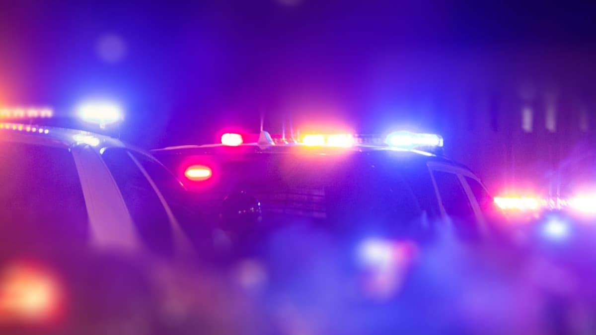 Blurred photo of police vehicles at night with red, blue, and amber emergency lights on