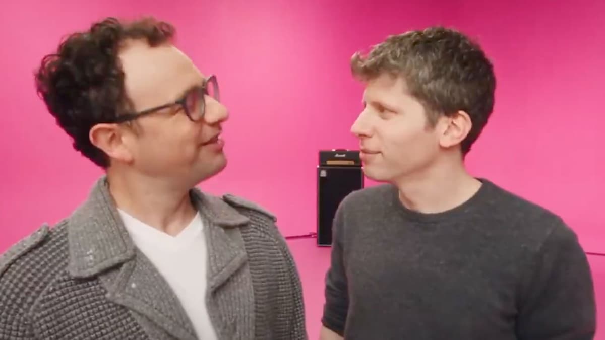 AI-generated version of the same shot: a man resembling Dario Amodei with curly hair, glasses, and a grey knit jacket on the left, face to face with a man resembling Sam Altman in a dark sweater on the right, same pink studio and amp