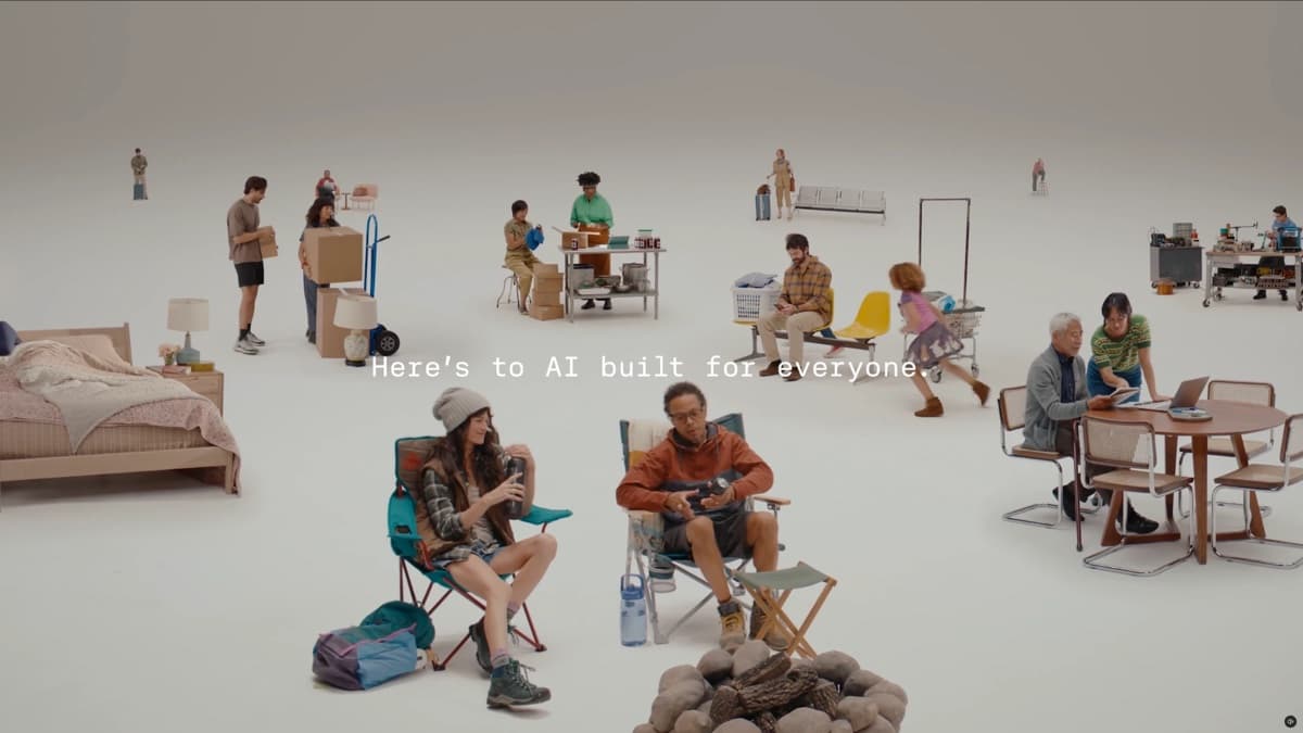 A white studio set with small vignettes of everyday life: people moving boxes, a cook at a prep table, a parent on a bench with a laundry basket, campers by a fire pit, an older couple at a laptop, and the caption 'Here's to AI built for everyone.'