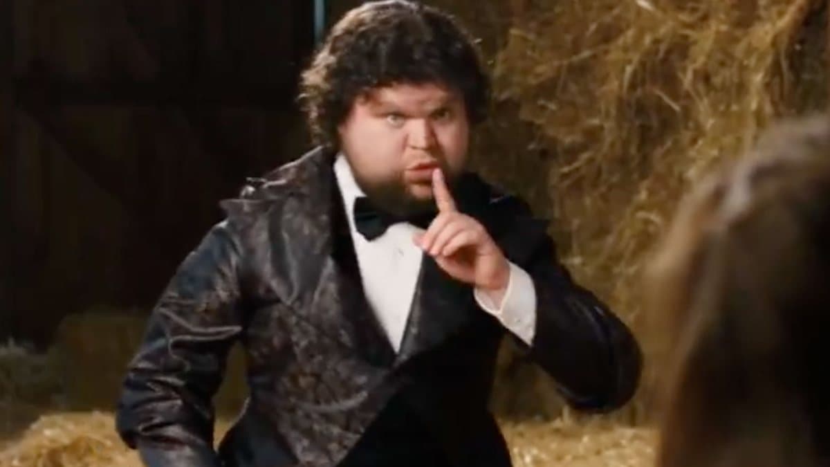AI remix of the tiptoe barn clip: a heavyset man with dark curly hair and a beard in the imp's brocade tuxedo and bow tie, finger raised to his lips, in front of hay bales