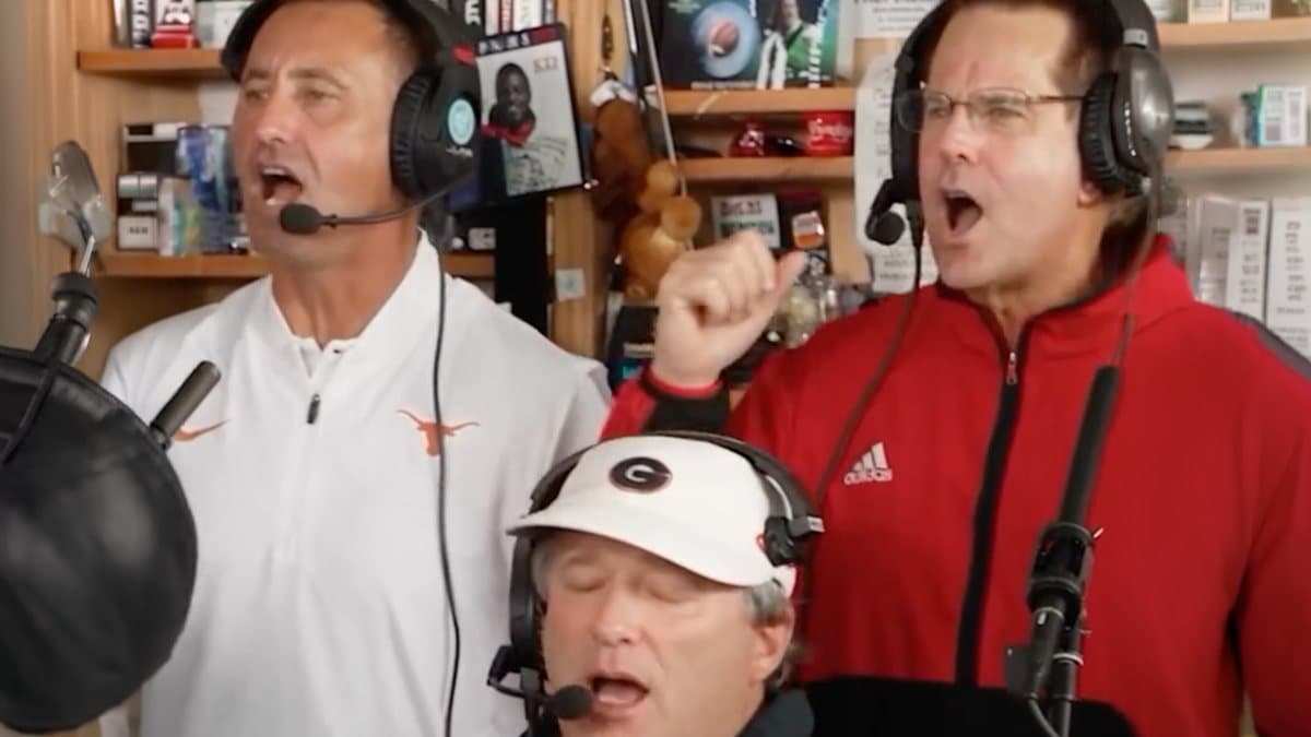 AI face-swap frame: Steve Sarkisian in a white Texas pullover, Kirby Smart in a Georgia cap, and a coach in a red Adidas jacket singing into Tiny Desk headset mics